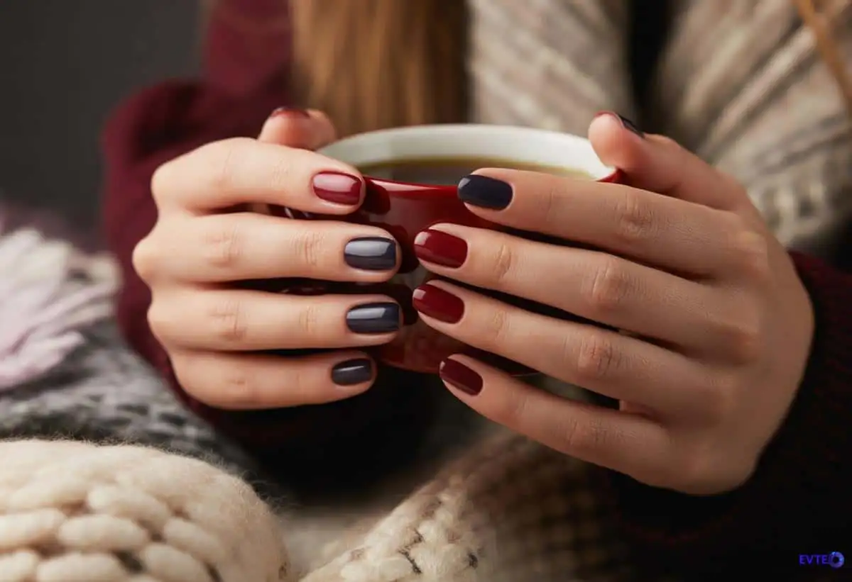 Mãos femininas elegantes com unhas escuras segurando uma xícara quente em um ambiente aconchegante de inverno