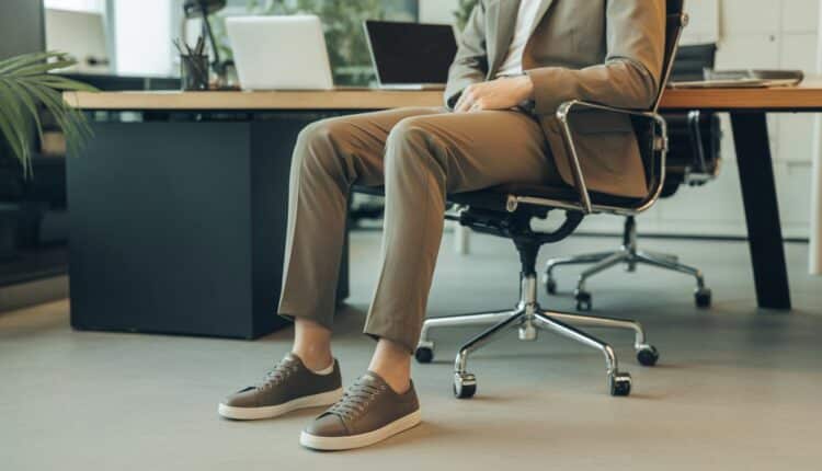 Pessoa vestindo tênis social com roupa de trabalho em um escritório moderno.